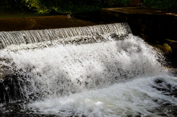 Natural stream of water. A small waterfall caused by man-made dam. Freeze shot of water falling from the waterfalls from the mountain to the lake.