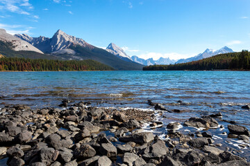 beautiful bright blue water of Maligne Lake with mountains in background, rocky shore in foreground