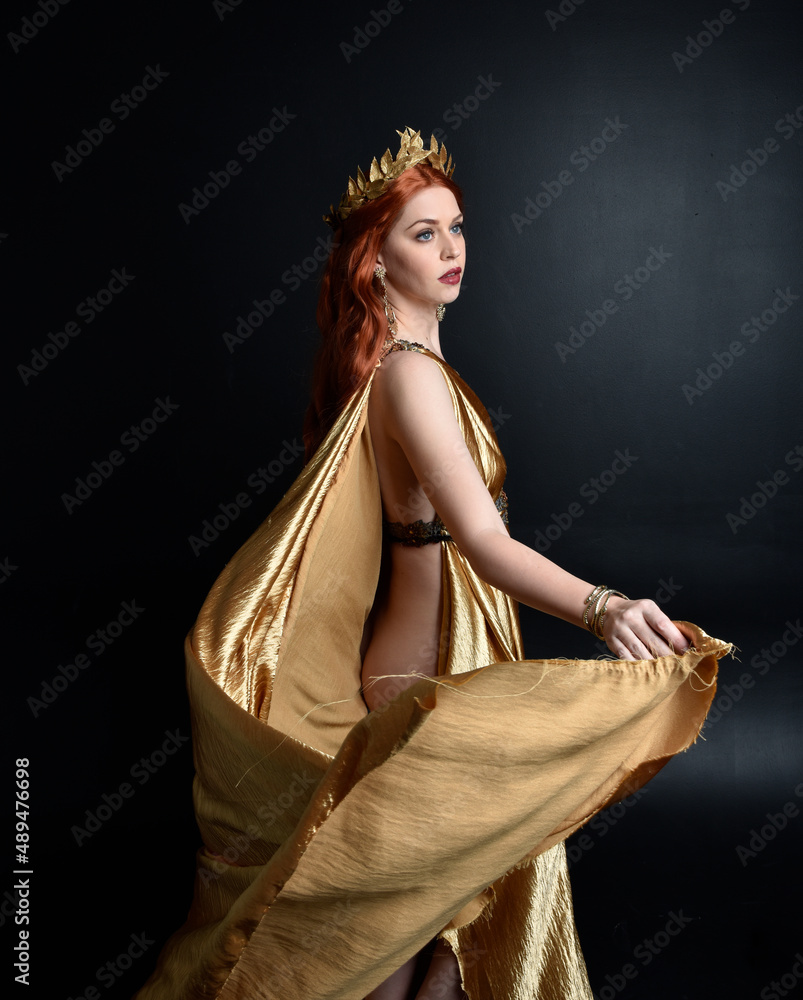 Poster  Full length portrait of pretty female model wearing  grecian goddess  toga gown, posing with elegant gestural movements on a studio background.