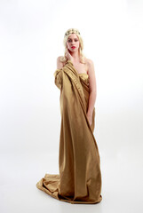 Naklejka premium Full length portrait of pretty female model wearing grecian goddess toga gown, posing with elegant gestural movements on a studio background.