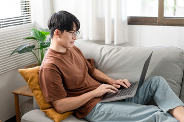 Fototapeta premium Technology Concept The man that is putting on glasses leaning his back on the dark yellow while focusing on the laptop’s screen