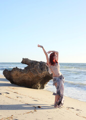  portrait of pretty female ship wrecked  model wearing  torn dress.  posing on the rocky  Ocean shoreline at sunset,