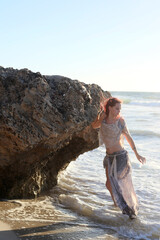  portrait of pretty female ship wrecked  model wearing  torn dress.  posing on the rocky  Ocean shoreline at sunset,