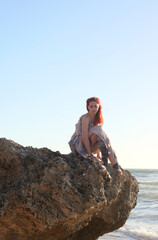  portrait of pretty female ship wrecked  model wearing  torn dress.  posing on the rocky  Ocean shoreline at sunset,