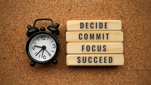 Alarm clock with text Decide, Commit, Focus and Succeed. Brown desk background. Conceptual