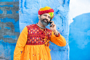 Happy north Indian mature man wearing colorful outfits and turban talking on smart phone, Smiling...