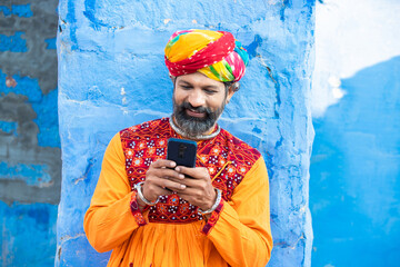 Happy north Indian mature man wearing colorful outfits and turban using smart phone, Smiling...
