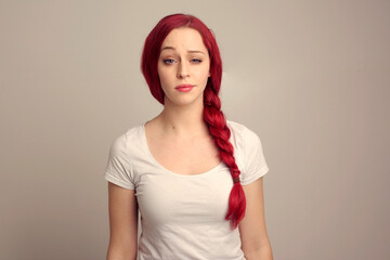 close up portrait of pretty female model with red hair in a braid, expressing emotion over the top facial expression on a studio background.