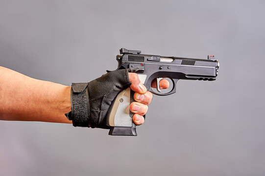 A man's hand holds a black pistol in his hand on a gray background