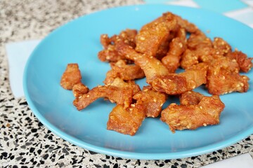 a crispy pork meat on bright blue dish in morning light, gravel table as background.
