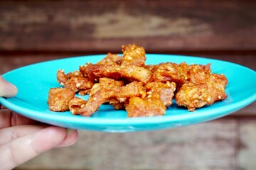 a crispy pork meat on bright blue dish in morning light, gravel table as background.