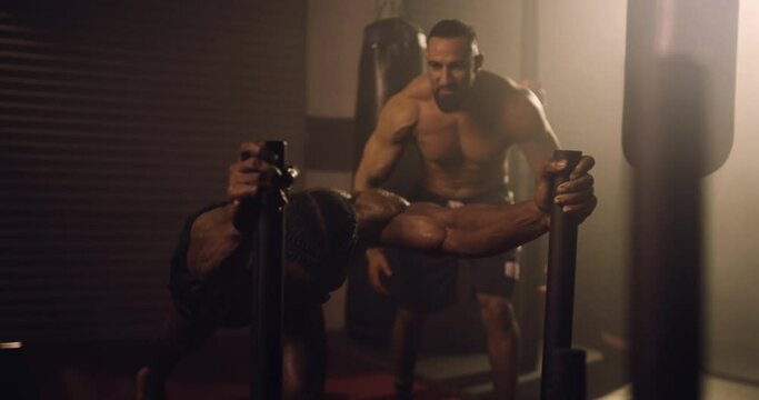 An African American Athlete and Hispanic Trainer Sled Push Training In A Gym. Shot In A Crossfit Boxing Gym With Low Key Lighting And A Scattering Of Haze. Captured On Red Digital Cinema Camera 