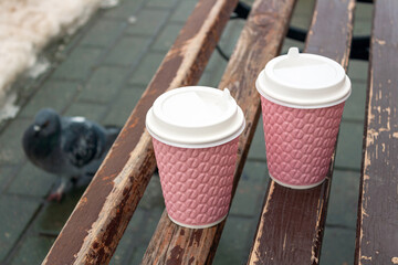 two cups of coffee stand on a wooden bench in the park, in early spring