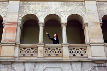 Full length portrait of red-haired woman wearing a  beautiful gothic gown costume, walking around  location with  romantic castle stone architecture background.