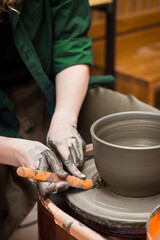 Potter's hands molds pot with tool close up. Woman works in pottery workshop. Clay bowl spinning on pottery wheel