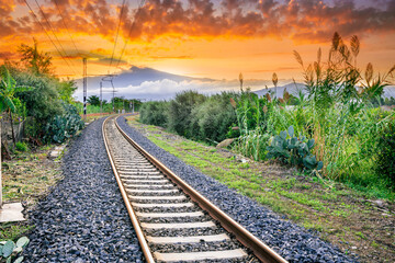 old evening railroad leading to a sunset glow in mountains with green bushes and cjlorful cloudy...