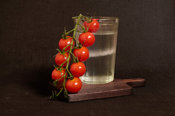 A faceted glass of vodka and a branch of cherry tomatoes on a wooden stand