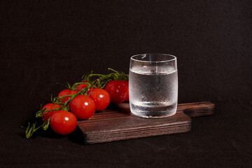 A glass of vodka and a branch of cherry tomatoes on a wooden stand