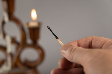 A man's hand holds an extinguished match against the burning candles. Brown ceramic candlestick in...