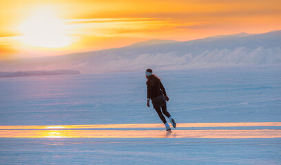 A young happy woman is skating on the transparent ice of the frozen Lake Baikal on a sunny winter...