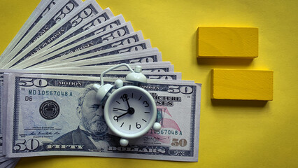 Top view of alarm clock with bank notes on yellow background. Copy space concept