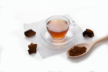 Chaga tea in a glass cup and pieces of chaga on a light background.
