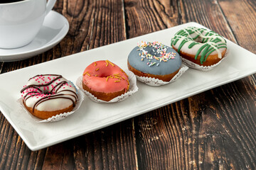 Delicious colorful mini donuts with coffee on wooden table