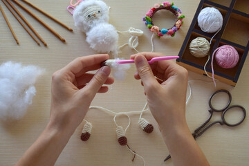 Making fanny sheep with wreath of flowers. Crochet toy ewe for child. On the table threads,...