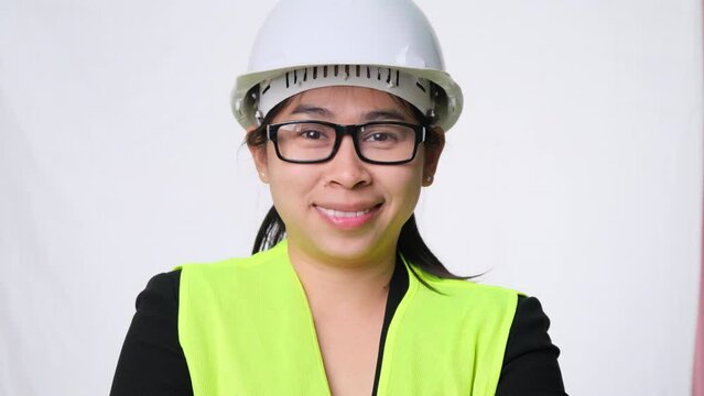 Smiling and confident female engineer wearing a helmet with her arms crossed over a white background in the studio.