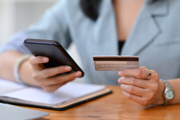 Close up view young woman holding credit card and making banking online or payment online on her smart phone.