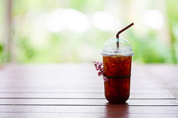 Plastic coffee mug, iced americano (black coffee) on a wooden table in the garden