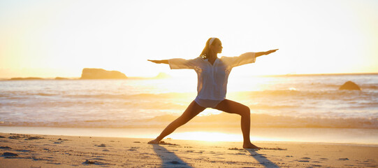 Tranquil and peaceful. Tranquil scene of a young woman doing a pilates pose on the beach at sunset.