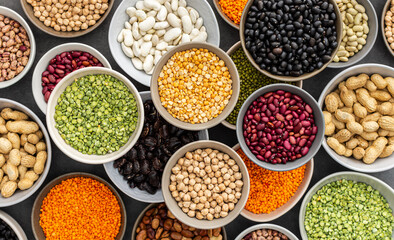 Different types of legumes in bowls, green with yellow peas and mung beans, chickpeas and peanuts, colored beans and lentils, top view - obrazy, fototapety, plakaty