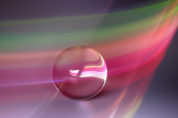 Glass ball and multicolored light on gray background