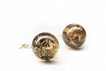Organic lichen earrings closeup. Natural dried plants inside transparent epoxy resin sphere balls with smooth surface. Selective focus on the details, object isolated on white background.