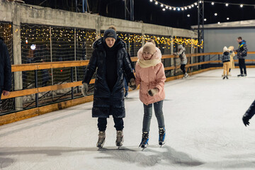 Obraz premium mother and daughter skate on the ice rink in the evening