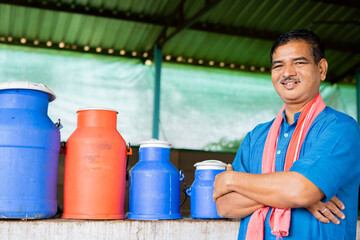 happy smiling diary farmer in front of milk containers at farm house with crossed arms by looking...
