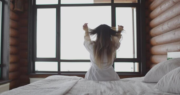 Back view of woman waking up and stretching hand on bed at wooden home. Slow motion