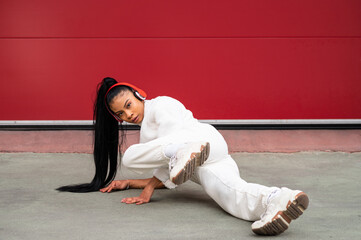 Cheerful African American woman with headphones
dancing urban dance on a red background