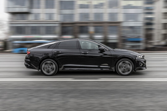 Black KIA K5 car in motion with urban blurred background