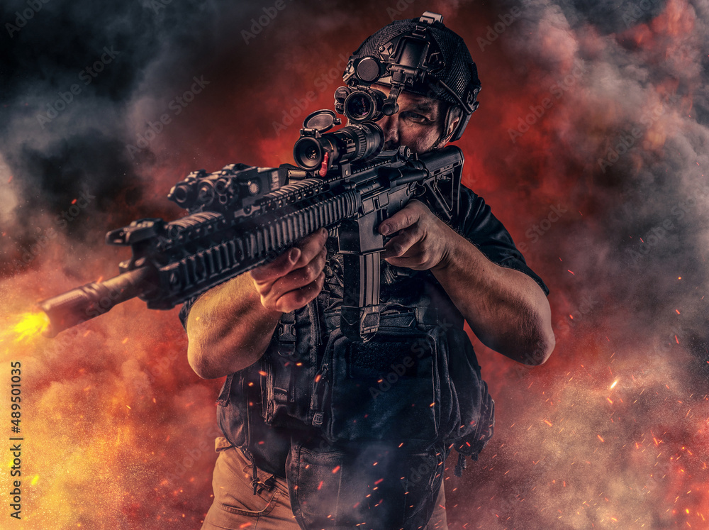 Wall mural Combative soldier with rifle shooting against fire explosions