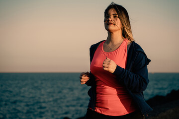 Active beautiful curvy woman jogging at sunset seaside - healthy lifestyle concept