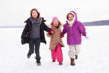 Lets go make snow angels. Three young sisters running outside in the snow.