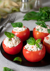Stuffed tomatoes with feta cheese and basil on black plate on light background. Close-up