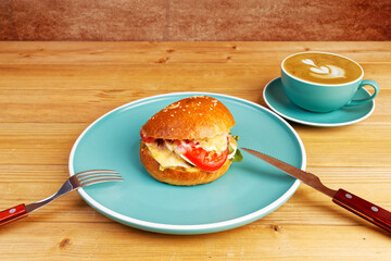 Bagel with chicken, tomato and cheese on wooden table.