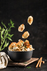 Fried dumplings with pork and herbs in a black round bowl and flying in the air
