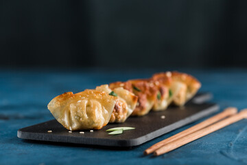 Fried dumplings with pork and greens on a black graphite board on a dark blue background with chopsticks.