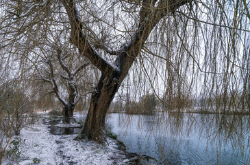 Winter landscape with two people walking alongside a snowy lake / river.