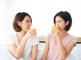 Asian pretty two girls drink homemade orange juice while looking each other in the morning at bedroom home