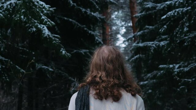 young man wearing blond long hair  walking and enjoying in  dense pine forest. Falling snow, warm winter day